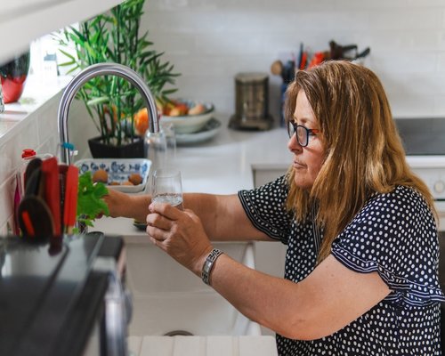 A person pouring a glass of clean water in a well-lit kitchen